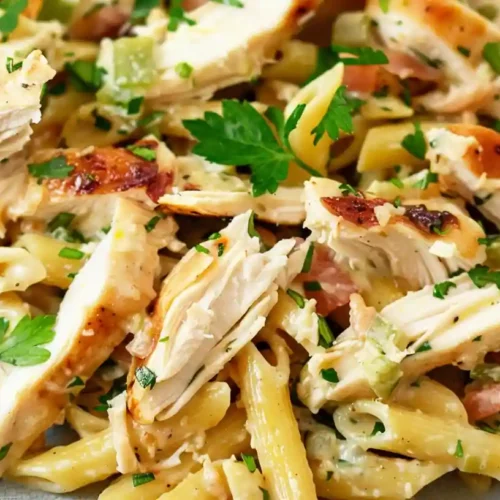 Creamy rotisserie chicken pasta with penne, bacon, herbs, and parmesan in a skillet.